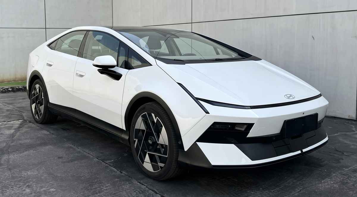 Fotografía frontal de registro del nuevo sedán Hyundai Ioniq V color blanco. Destaca su diseño tipo fastback con líneas afiladas, faros delgados integrados, rines aerodinámicos bitono y un robusto parachoques inferior negro mate.