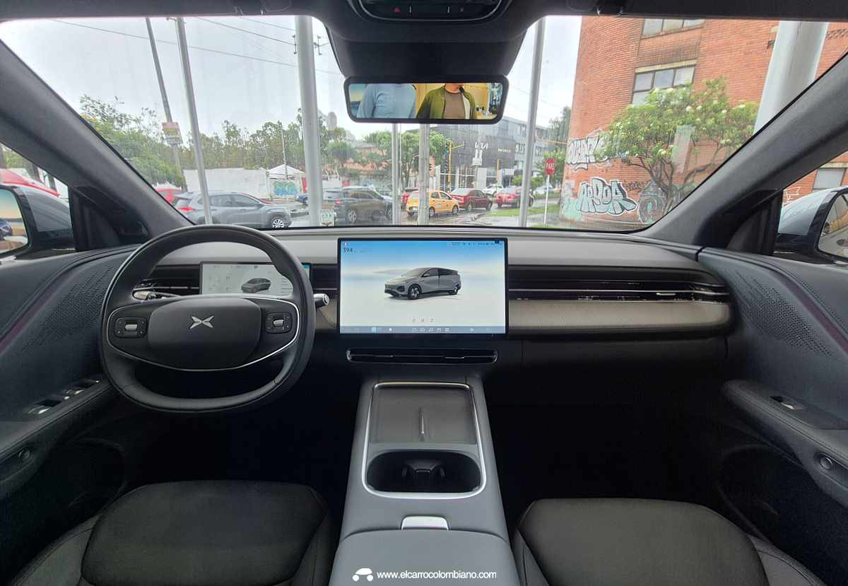 Interior de la cabina de la Xpeng G6, mostrando el volante multifunción, el cuadro de instrumentos digital y la gran pantalla táctil central proyectando el vehículo, con vista hacia la calle desde la vitrina.
