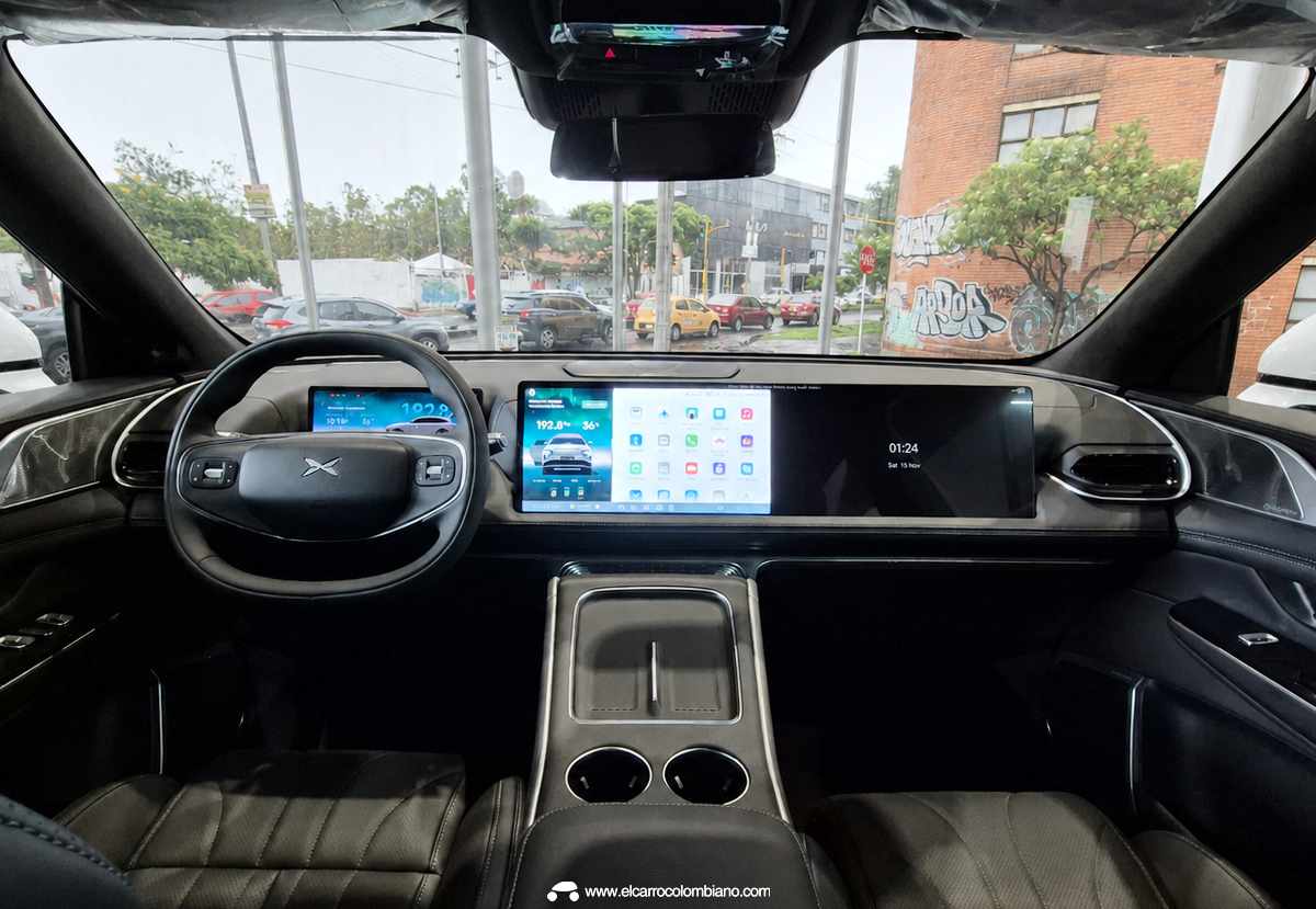 Puesto de conducción de la Xpeng G9, destacando su lujoso interior oscuro, amplia consola central con doble cargador y las enormes pantallas digitales extendidas sobre el tablero multifunción.