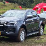 Vista frontal en tres cuartos de la nueva Isuzu Pickup 2027 color gris oscuro sobre una pista de barro, destacando su nueva parrilla y faros rediseñados en Colombia.