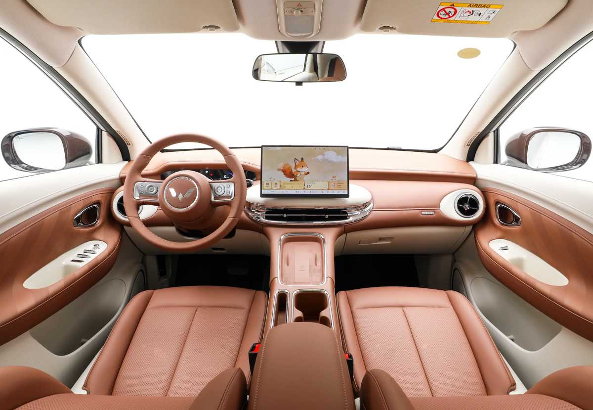 Diseño interior minimalista del Wuling Binguo Pro, resaltando su elegante tapicería en tonos caramelo, volante de estilo clásico y una gran pantalla táctil central flotante.