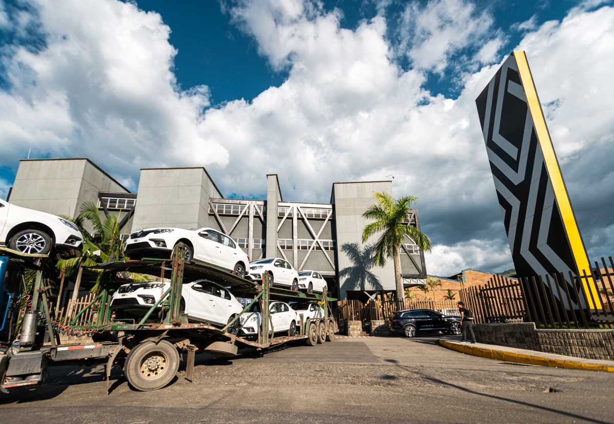 Camión niñera cargado con vehículos Renault nuevos de color blanco, saliendo de la planta de producción listos para su distribución y exportación.