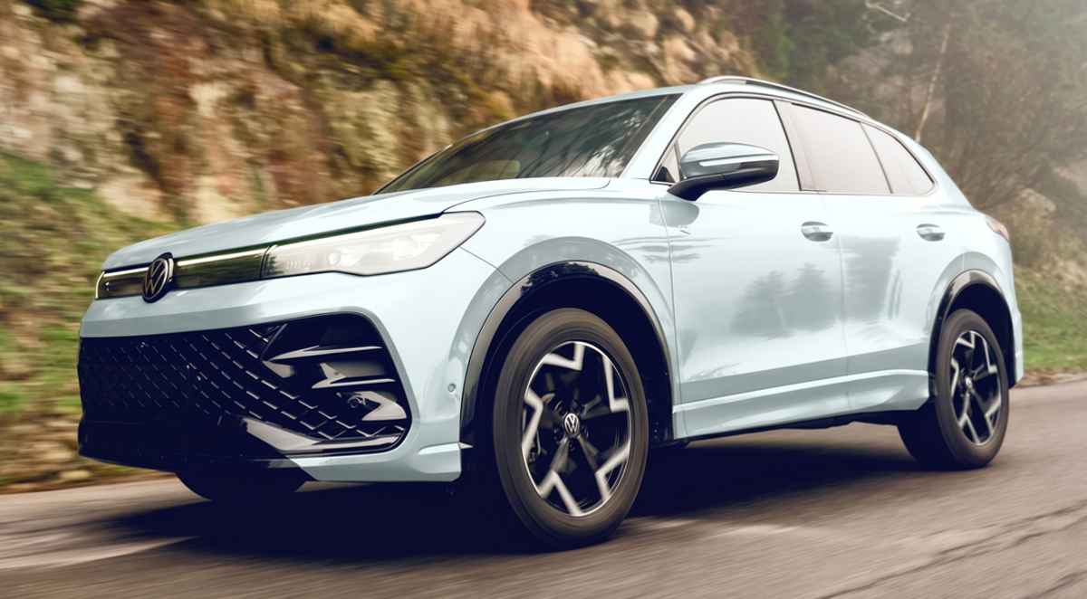 Nueva Volkswagen Tiguan e-TSI híbrida color blanco puro en movimiento sobre una carretera de montaña, destacando su renovado diseño frontal y rines aerodinámicos bitono.