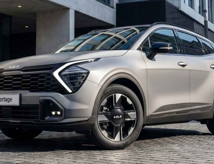 Kia Sportage HEV color plata mate estacionada sobre una calle adoquinada con arquitectura urbana moderna de fondo, destacando su imponente parrilla oscura y luces diurnas LED en forma de búmeran.
