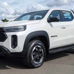 Vista tres cuartos delantera de la nueva pick-up RAM Dakota color Blanco Glaciar, destacando su parrilla frontal oscura y diseño robusto, estacionada a plena luz del día.