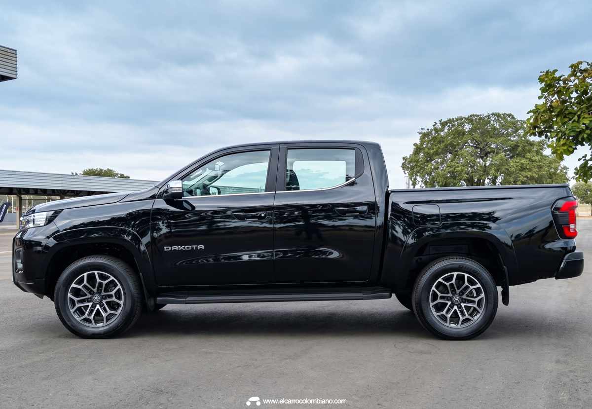 Perfil lateral completo de la camioneta RAM Dakota color Negro Diamante, exhibiendo sus rines de aleación oscurecidos, estribos laterales y altura libre al suelo de 22,8 cm.