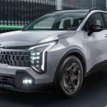 Camioneta Kia Sportage color plata en movimiento por una vía urbana moderna, destacando sus luces LED diurnas y diseño frontal.