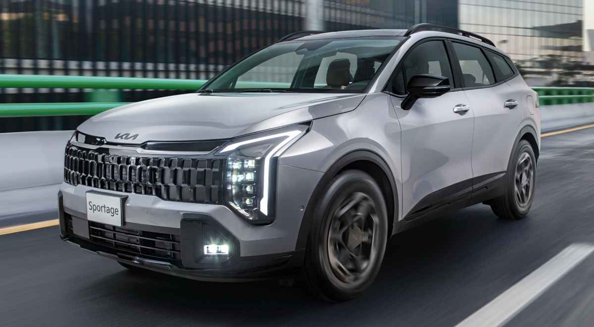 Camioneta Kia Sportage color plata en movimiento por una vía urbana moderna, destacando sus luces LED diurnas y diseño frontal.