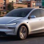 Automóvil Tesla color plata transitando a gran velocidad por una vía en Colombia, con un letrero de señalización hacia la Autopista Sur de Medellín en el fondo.