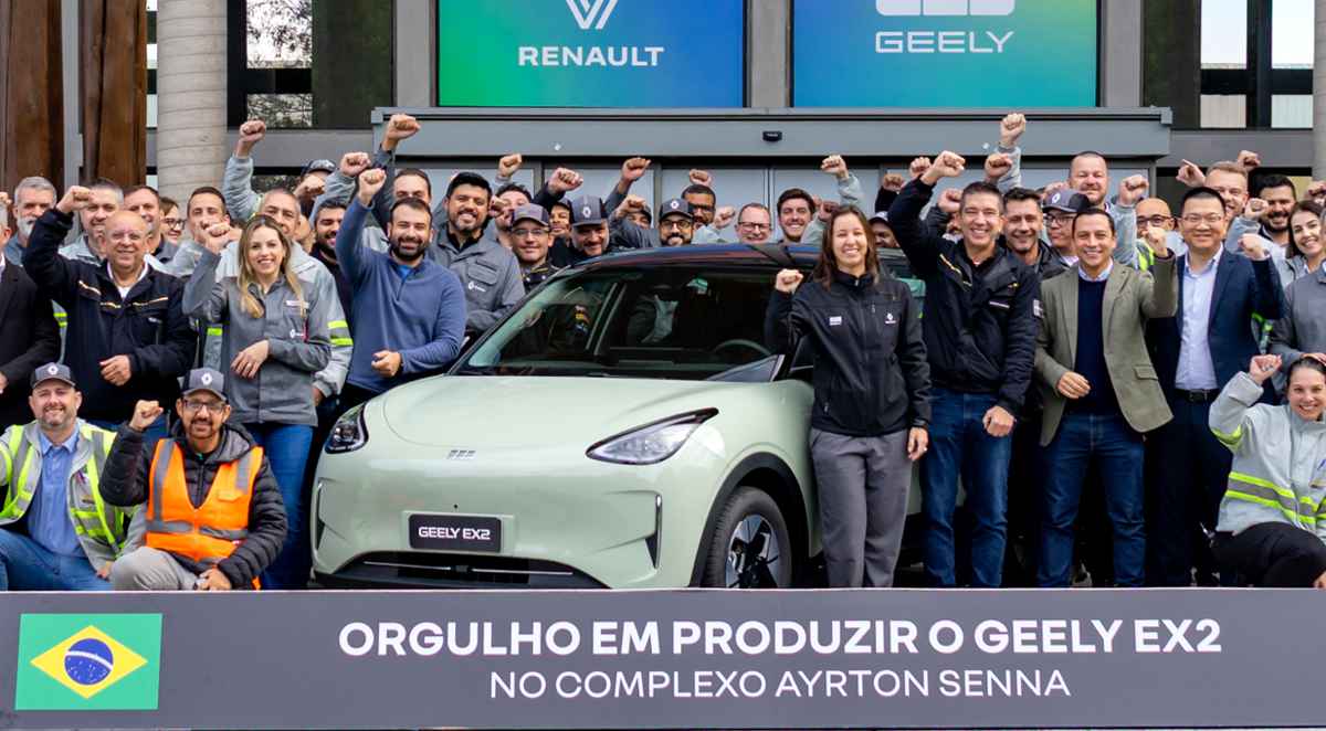 Grupo de directivos y trabajadores celebrando junto al carro eléctrico Geely EX2 color verde claro en el Complejo Ayrton Senna en Brasil, con logotipos de Renault y Geely en el fondo y un cartel conmemorativo de su producción sudamericana.