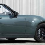 Vista lateral delantera del deportivo Mazda MX-5 convertible luciendo la nueva pintura exterior Verde Zinc, contrastando con sus rines negros y techo de lona gris.