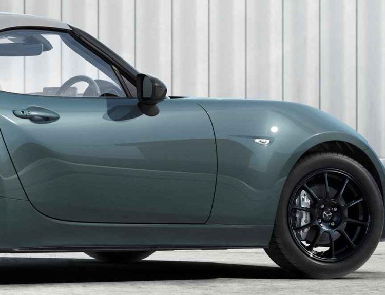 Vista lateral delantera del deportivo Mazda MX-5 convertible luciendo la nueva pintura exterior Verde Zinc, contrastando con sus rines negros y techo de lona gris.
