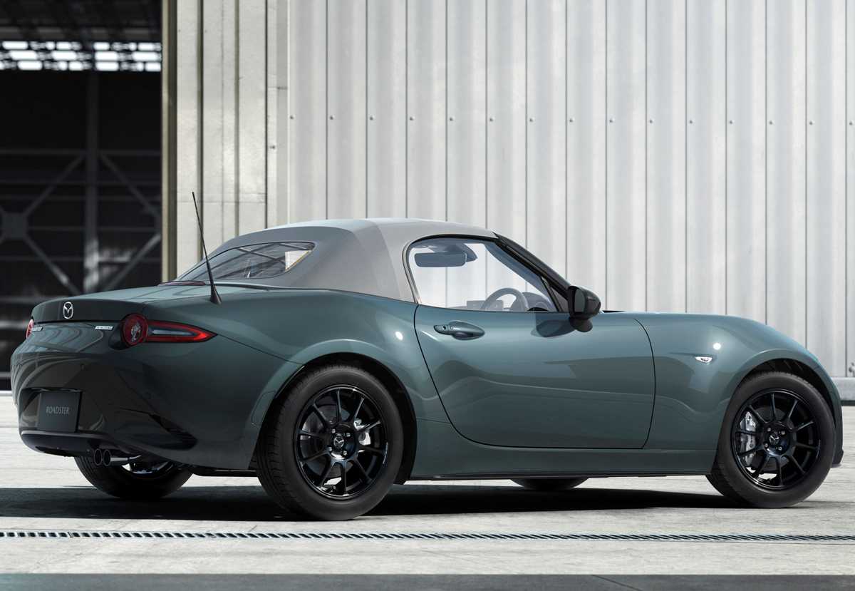 Vista tres cuartos trasera del Mazda MX-5 con techo de lona gris, destacando las líneas de diseño bajo la nueva pintura Verde Zinc y sus rines de aleación oscuros.