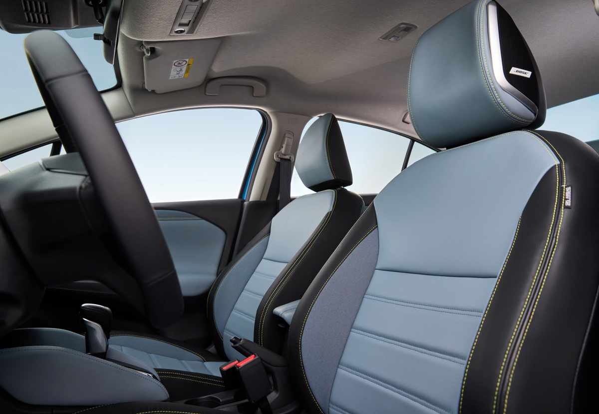 Asientos delanteros del Nissan Versa 2027 tapizados en cuero-vinilo y tela gris, destacando los parlantes Bose integrados en el apoyacabezas del conductor.