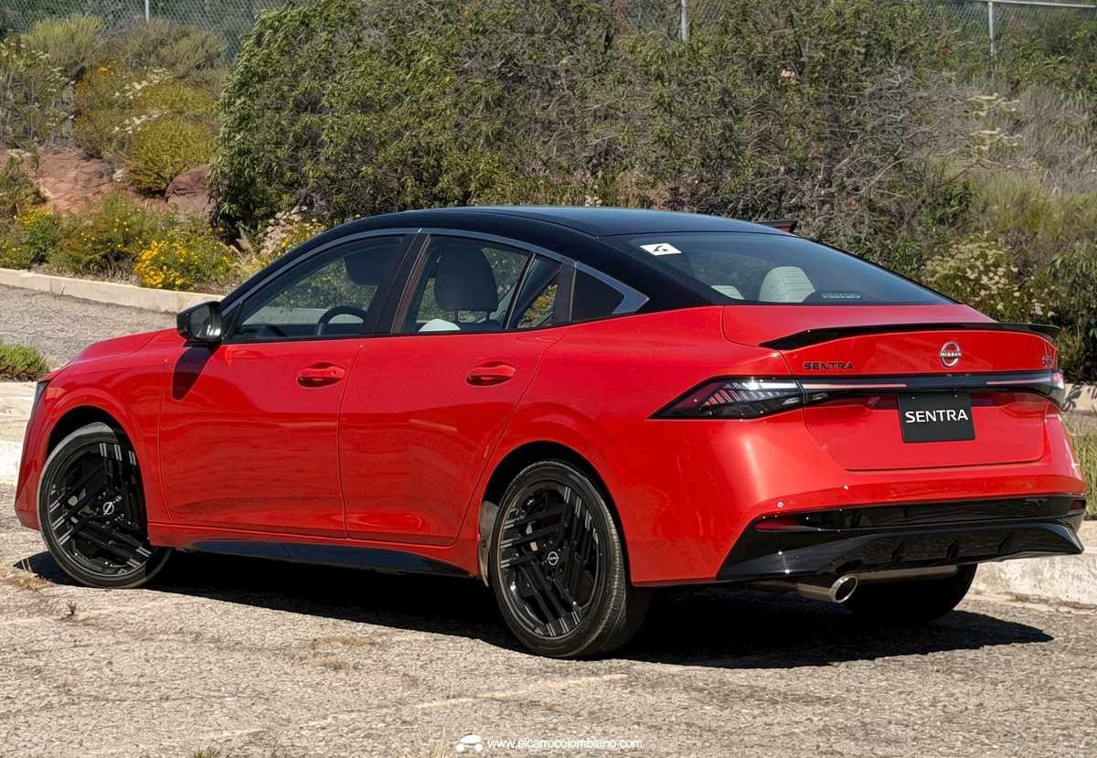 Perspectiva tres cuartos trasera del Nissan Sentra 2027 color naranja, luciendo su pronunciada caída de techo tipo fastback, spoiler trasero negro y la firma lumínica LED interconectada.