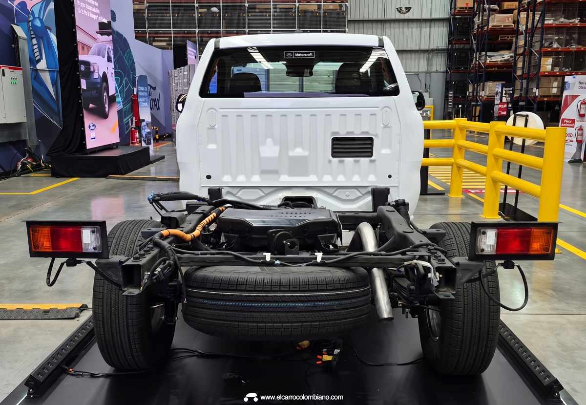 Vista técnica detallada desde la parte posterior del chasís desnudo de la Ford Ranger, revelando el eje rígido, las ballestas, la llanta de repuesto y las luces traseras provisionales instaladas de fábrica.