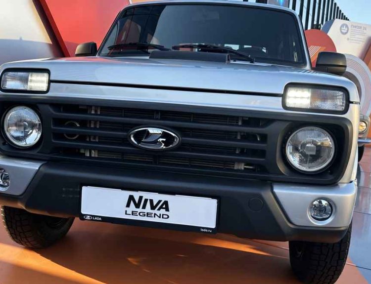 Vista frontal detallada del renovado Lada Niva Legend 2026 color plata exhibido en un evento, destacando su clásica parrilla negra, faros redondos y la nueva toma de aire funcional sobre el capó.