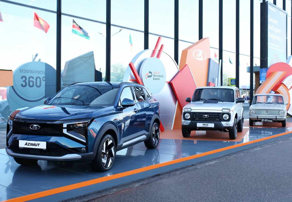 El clásico Lada Niva Legend exhibido en un gran stand corporativo junto al moderno y tecnológico SUV Lada Azimut de color azul profundo, y el histórico sedán VAZ-2101 blanco al fondo.