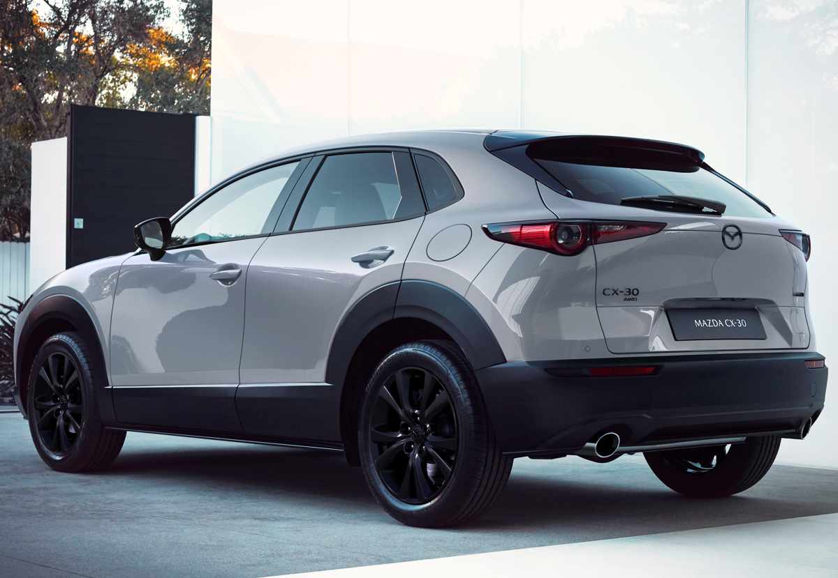 Perspectiva trasera de tres cuartos de la Mazda CX-30 2027, mostrando la caída del techo, los protectores plásticos en los pasos de rueda y sus luces traseras LED deportivas.