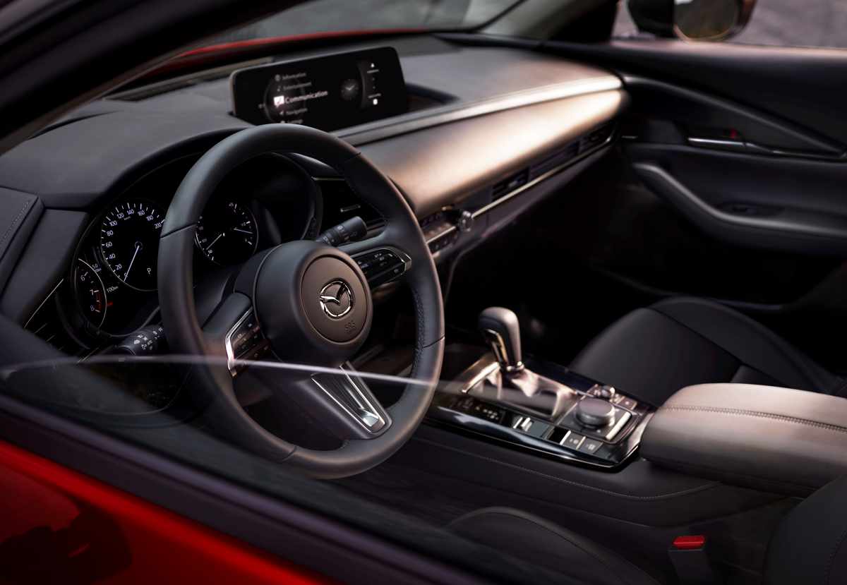 Diseño interior del habitáculo de la Mazda CX-30 2027, enfocado en el puesto del conductor con el volante multifunción de cuero y la renovada pantalla central de 10,25 pulgadas.