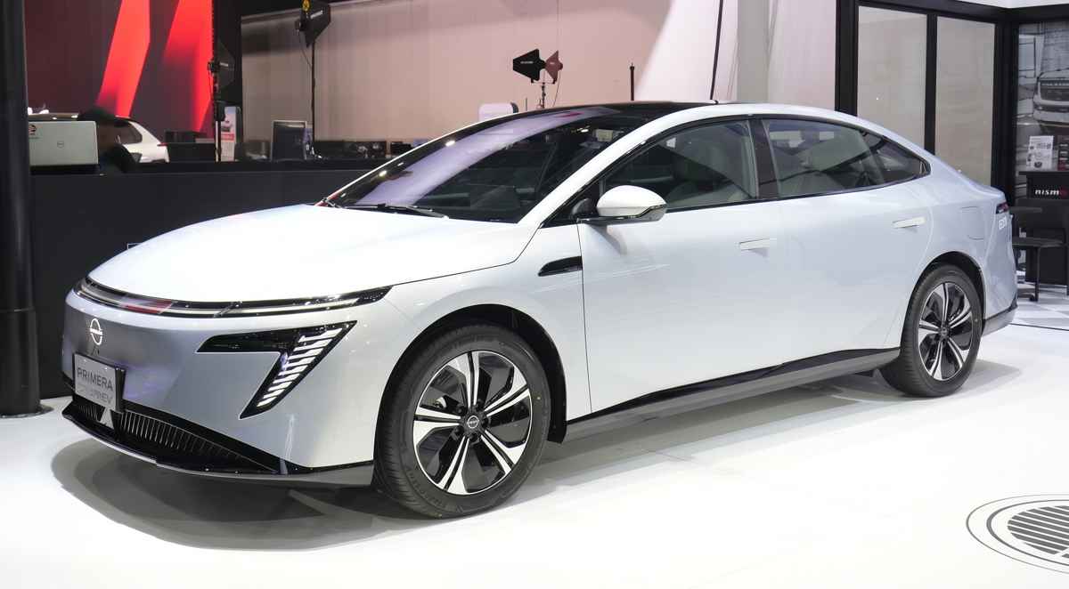 Vista frontal de tres cuartos del nuevo sedán eléctrico Nissan Primera EV en color blanco, exhibido en un salón del automóvil destacando su silueta aerodinámica y rines bitono.