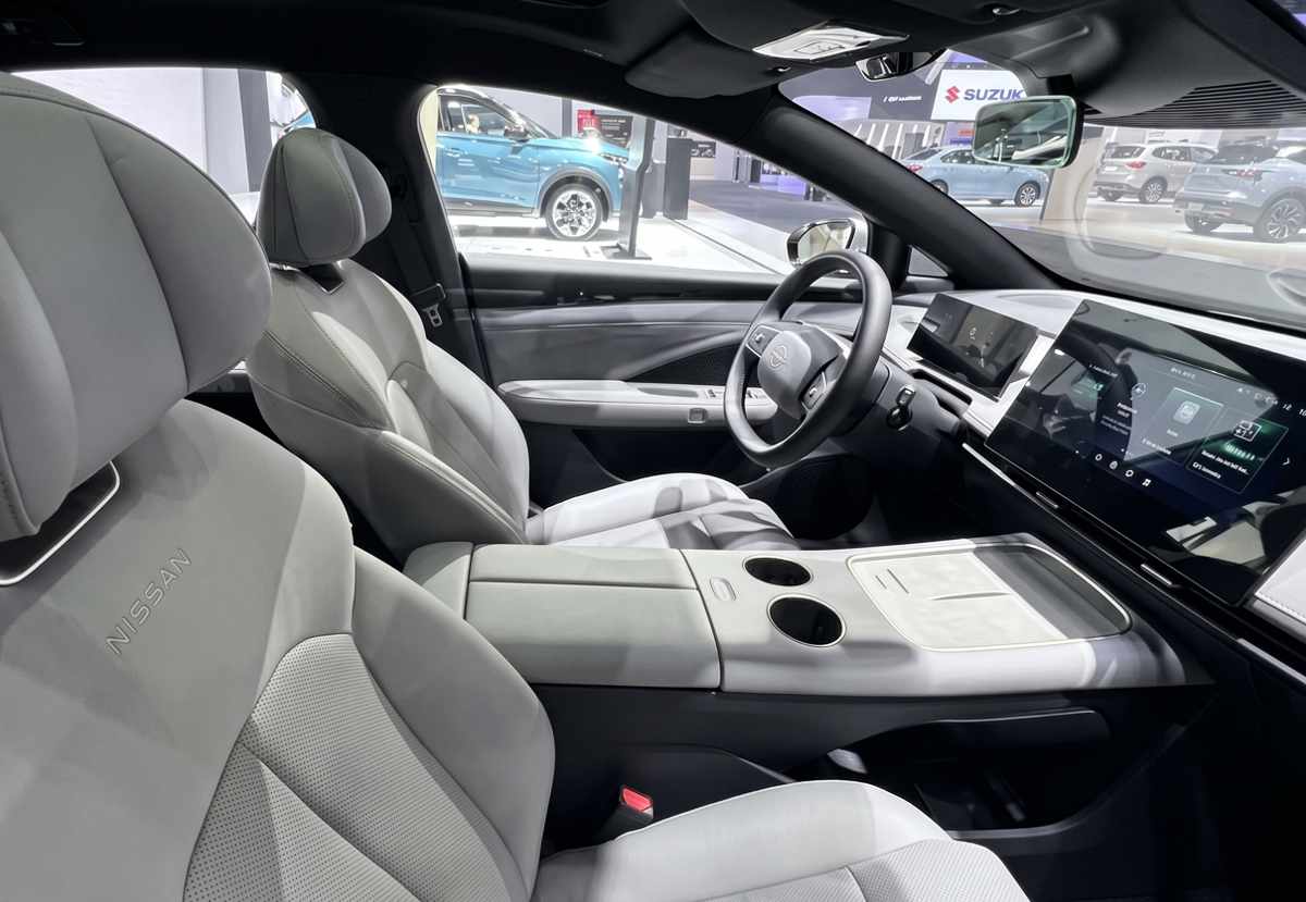 Diseño del habitáculo interior del Nissan Primera EV, mostrando los asientos de cuero gris claro con la inscripción de la marca, el volante de dos radios y la pantalla flotante del centro multimedia.