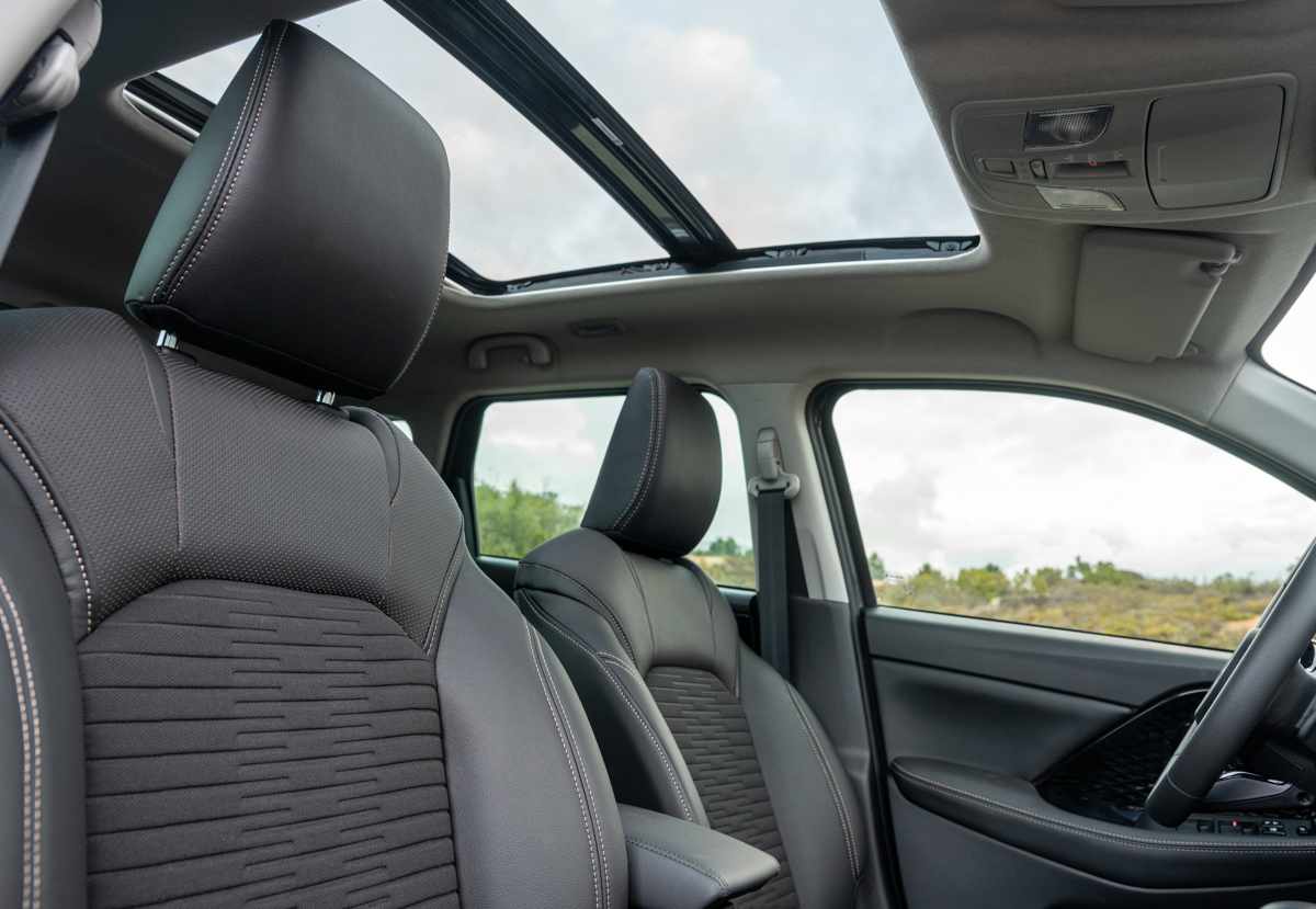 Vista interior superior de la Suzuki Across detallando el techo corredizo eléctrico abierto y los contornos de los asientos tapizados en cuero sintético oscuro.