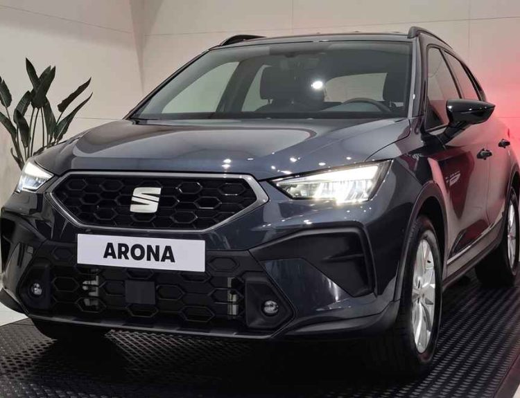 Vista frontal de tres cuartos de la renovada SUV SEAT Arona Style color Gris Magnético exhibida en vitrina, destacando su nueva parrilla hexagonal y firma lumínica LED.
