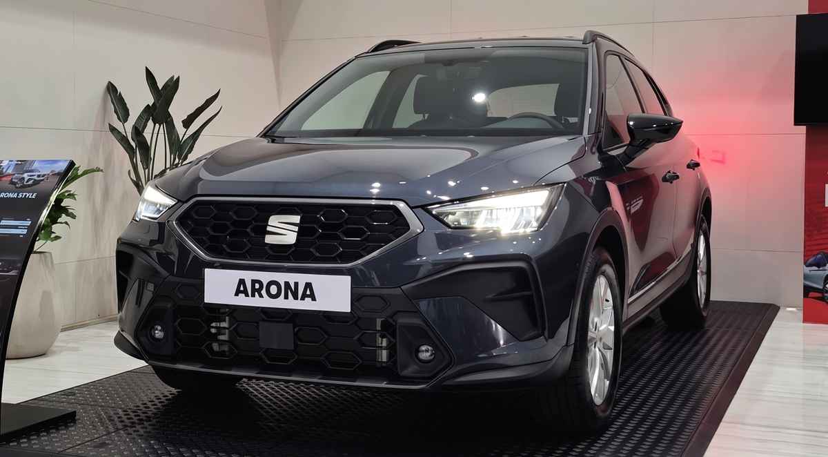 Vista frontal de tres cuartos de la renovada SUV SEAT Arona Style color Gris Magnético exhibida en vitrina, destacando su nueva parrilla hexagonal y firma lumínica LED.