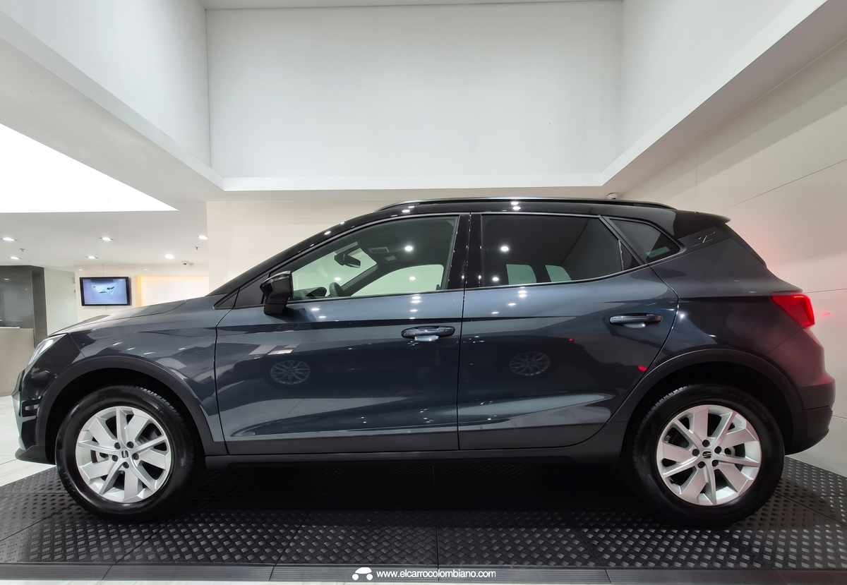 Perfil lateral completo de la SUV SEAT Arona Style color Gris Magnético, exhibiendo su carrocería bitono con barras portaequipaje y rines de aleación de aluminio de 16 pulgadas.