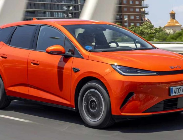 Vista frontal en movimiento del BYD Dolphin G DM-i híbrido enchufable color naranja recorriendo una vía urbana, mostrando su diseño aerodinámico.