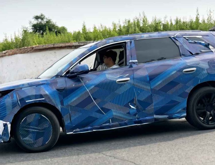 Vista de perfil en marcha de la nueva generación del BYD Tang cubierta con un denso camuflaje azul con patrones geométricos durante pruebas de ruta en China.