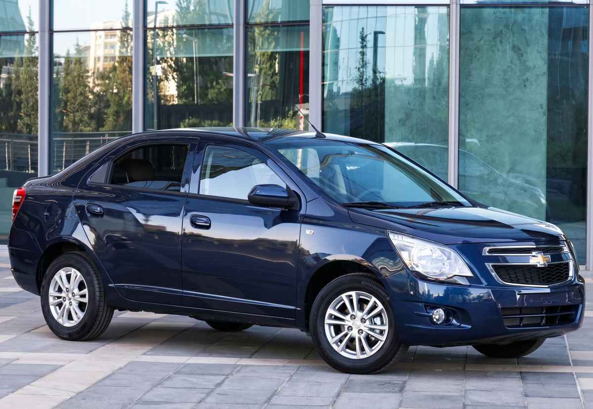 Fotografía de un sedán Chevrolet Cobalt de color azul oscuro estacionado frente a un edificio de fachadas de vidrio en Uzbekistán, el carro más vendido en dicho país asiático.