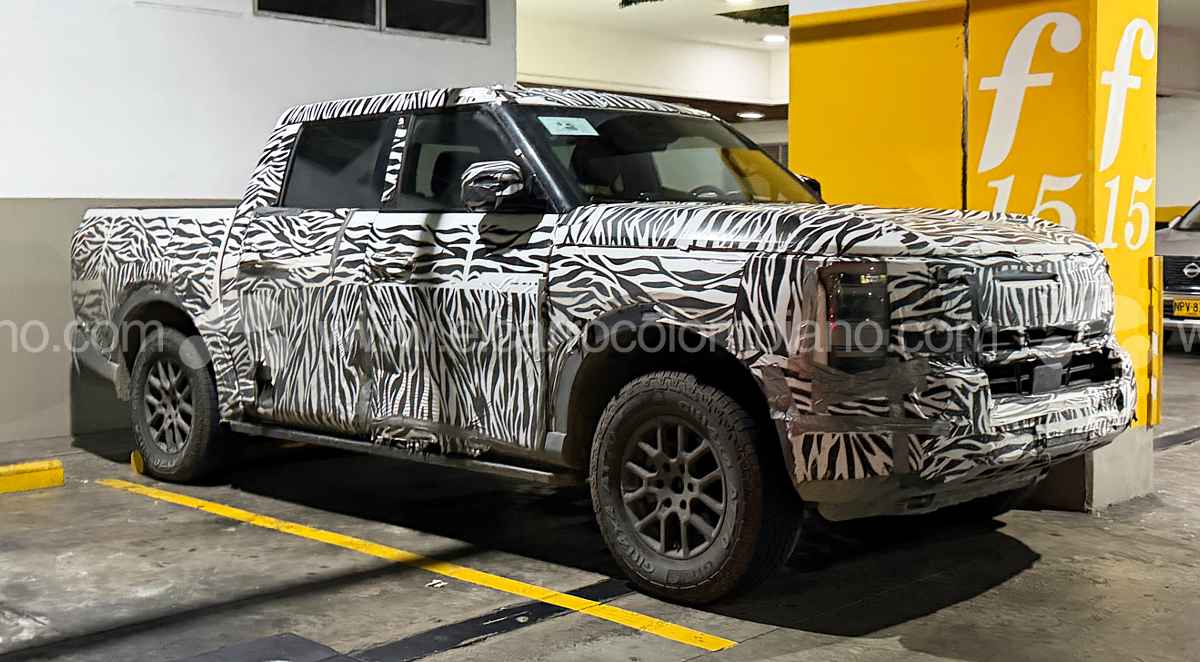 Vista lateral y frontal de tres cuartos de la nueva pick-up Nissan Frontier Pro híbrida enchufable cubierta con camuflaje de cebra, estacionada en un parqueadero en Bucaramanga durante sus pruebas de ruta.