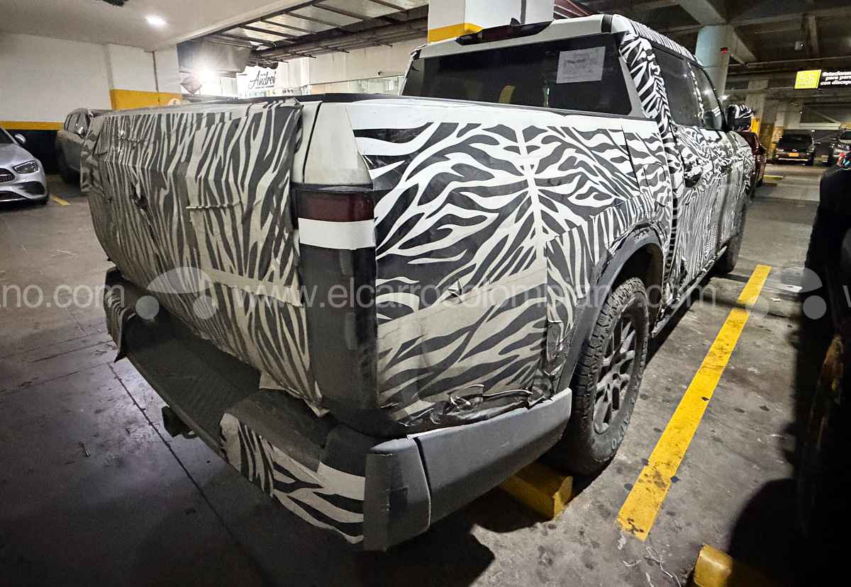 Perspectiva trasera de la Nissan Frontier Pro PHEV en pruebas, mostrando el platón cubierto, las líneas de la compuerta y el diseño vertical de los stops bajo el camuflaje.