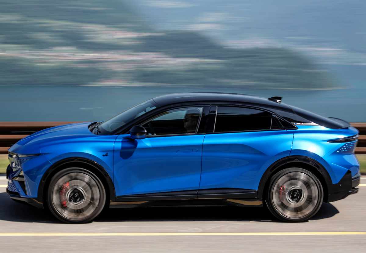 Perfil dinámico del SUV deportivo Alpine A390 GTS azul rodando en carretera junto a un lago, evidenciando su bajísimo centro de gravedad y la fluidez de sus líneas.