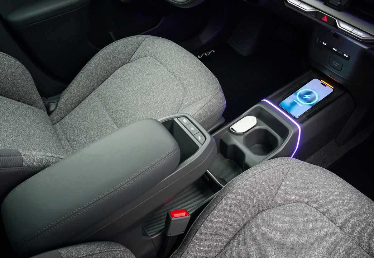 Consola central del habitáculo del Kia EV2 mostrando el cargador inalámbrico para celulares con iluminación ambiental, posavasos y apoyabrazos delantero.
