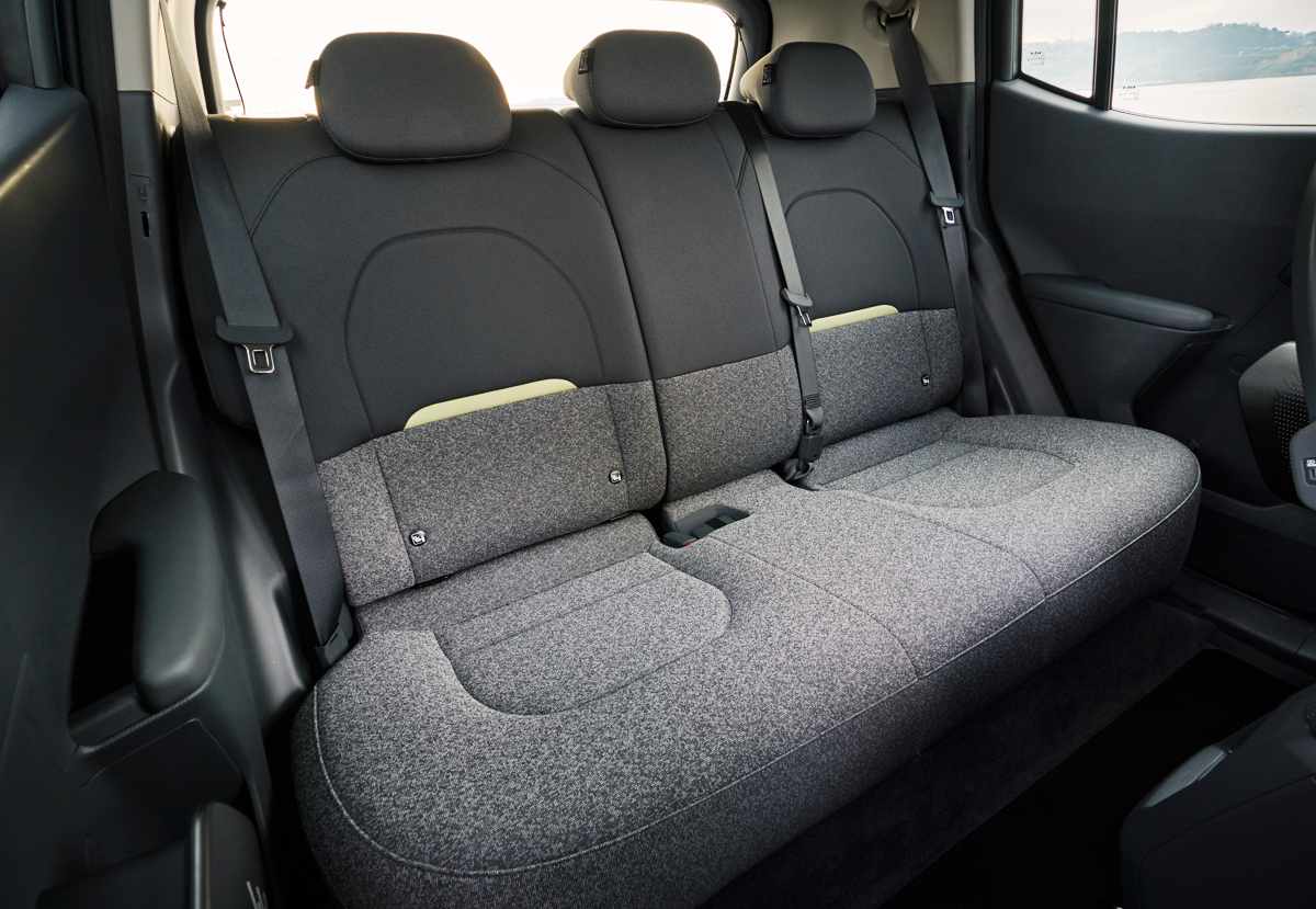 Asientos traseros del Kia EV2 tapizados en tela gris con respaldos abatibles 60/40, evidenciando el espacio interior para tres pasajeros.