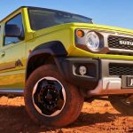 Vista en plano contrapicado tres cuartos del Suzuki Jimny XL Rhino Special Edition color Amarillo Cinético en un terreno desértico, destacando su parrilla clásica y rines negros.