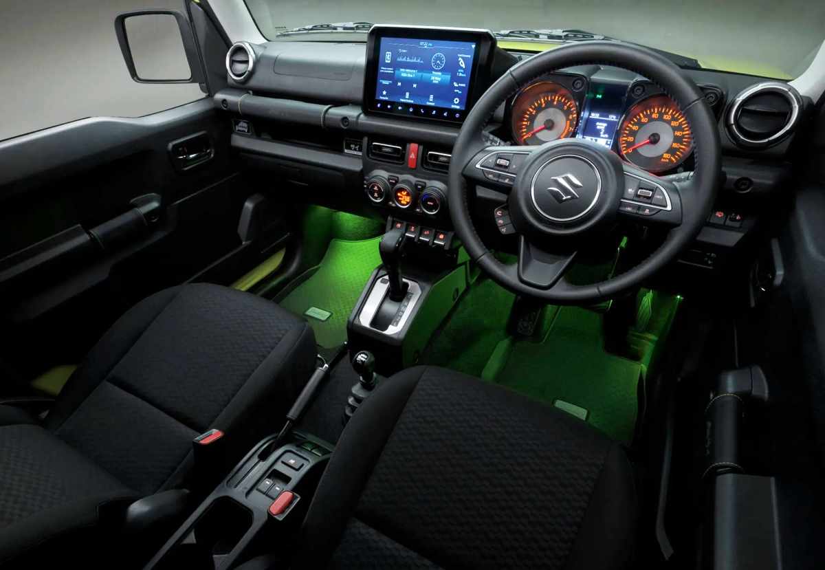 Cabina interior del Suzuki Jimny XL Rhino con el volante a la derecha, mostrando la pantalla multimedia de nueve pulgadas y la iluminación ambiental verde para el piso.