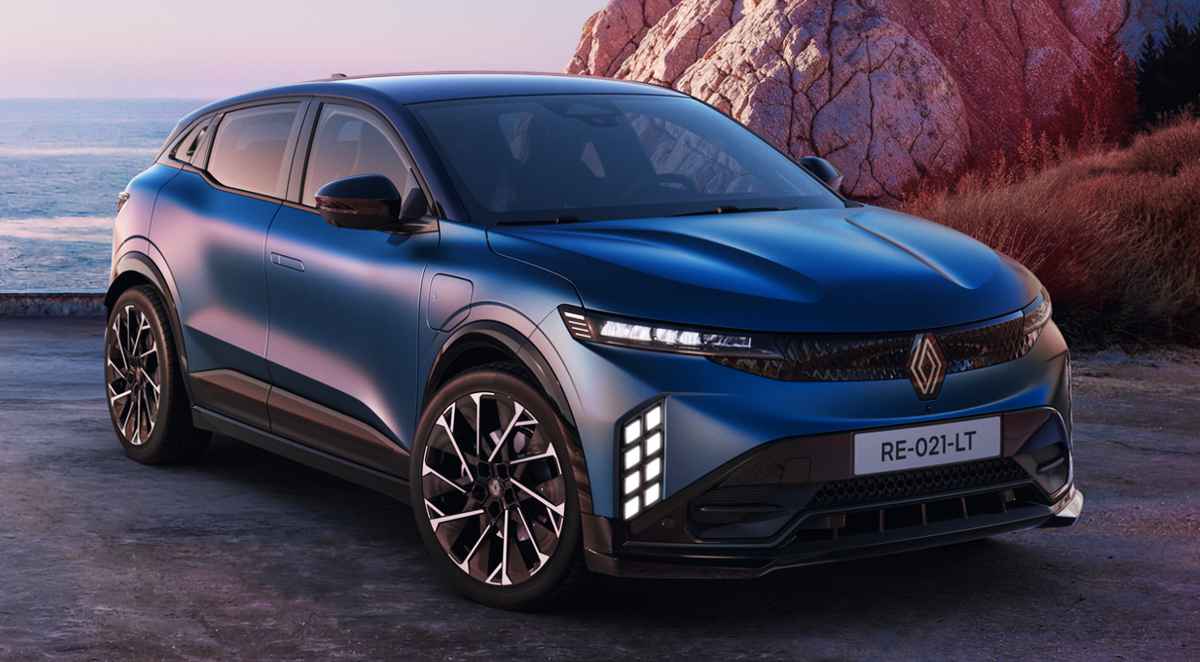 Vista frontal de tres cuartos del nuevo Renault Mégane E-Tech 2027 color azul satinado estacionado junto a la costa, destacando su nueva parrilla oscura y luces diurnas verticales.