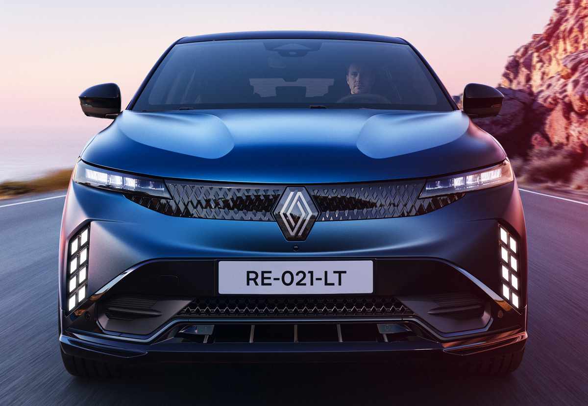 Primer plano frontal del Renault Mégane E-Tech 2027 en movimiento sobre una carretera costera, detallando el patrón lumínico de sus nuevas luces diurnas LED y el emblema del rombo.