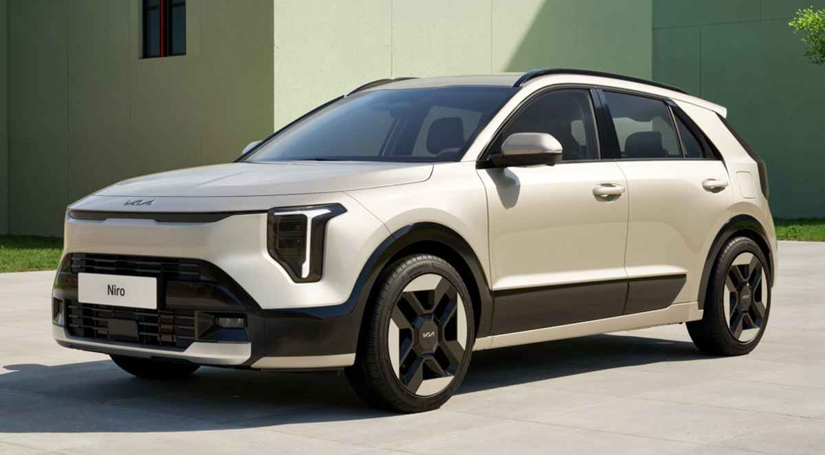 Vista frontal tres cuartos de la nueva SUV híbrida Kia Niro 2027 color beige estacionada frente a un edificio moderno a la luz del día, destacando sus nuevas luces diurnas LED en forma de T y rines aerodinámicos.