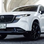 Vista frontal en ángulo bajo de la nueva generación de la SUV Mazda CX-5 en color blanco, destacando su gran parrilla delantera negra con detalles oscuros, rines oscuros de aleación y placas de matriculación japonesas bajo un puente.