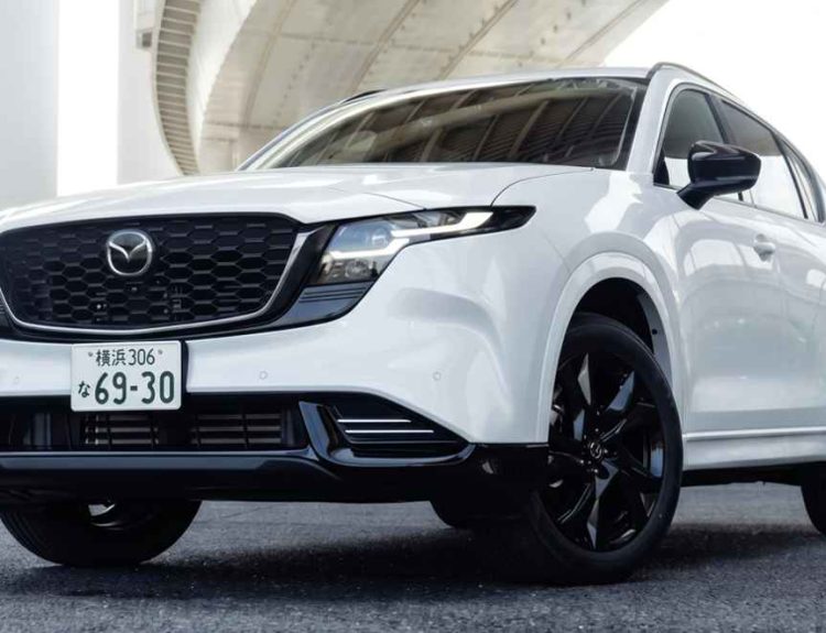 Vista frontal en ángulo bajo de la nueva generación de la SUV Mazda CX-5 en color blanco, destacando su gran parrilla delantera negra con detalles oscuros, rines oscuros de aleación y placas de matriculación japonesas bajo un puente.