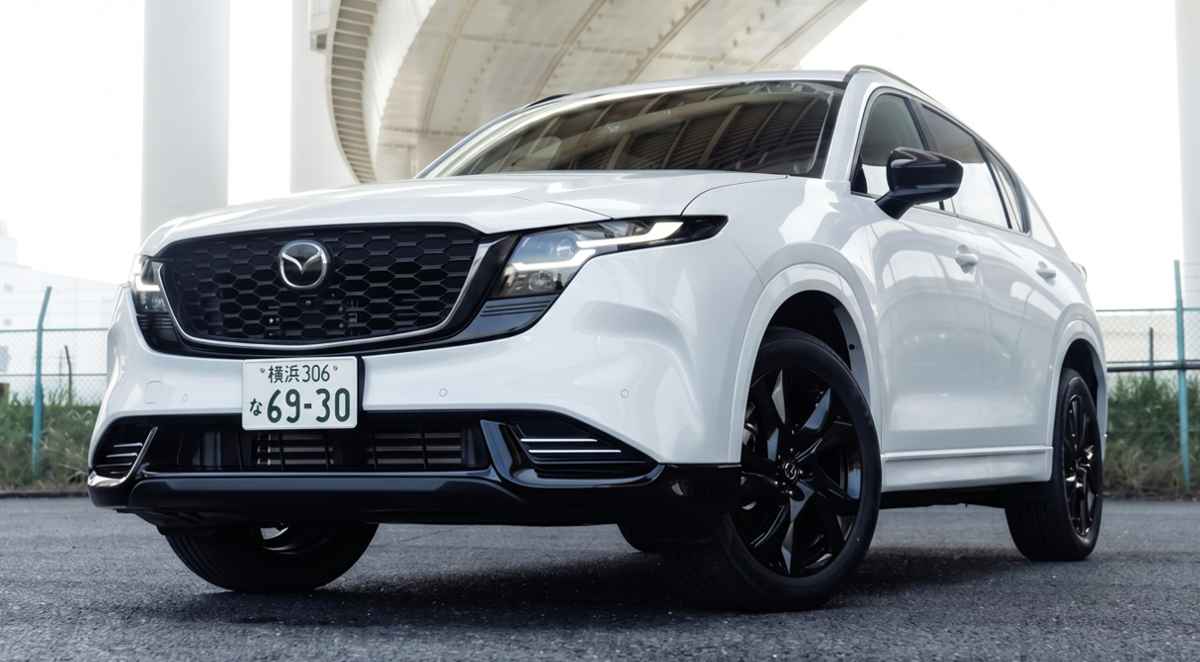 Vista frontal en ángulo bajo de la nueva generación de la SUV Mazda CX-5 en color blanco, destacando su gran parrilla delantera negra con detalles oscuros, rines oscuros de aleación y placas de matriculación japonesas bajo un puente.