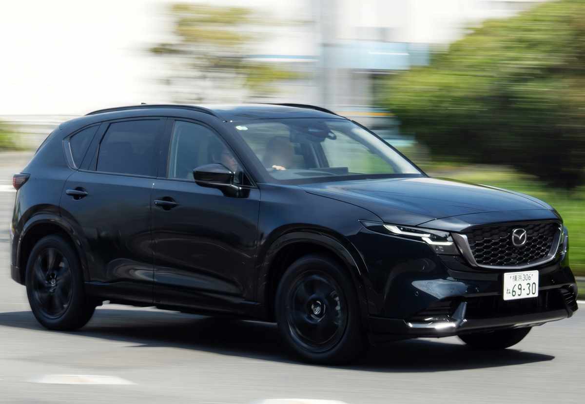 Fotografía en movimiento de la nueva SUV Mazda CX-5 en color negro, mostrando su perfil lateral dinámico, líneas aerodinámicas de la carrocería y rines negros en una vía pública con fondo difuminado.