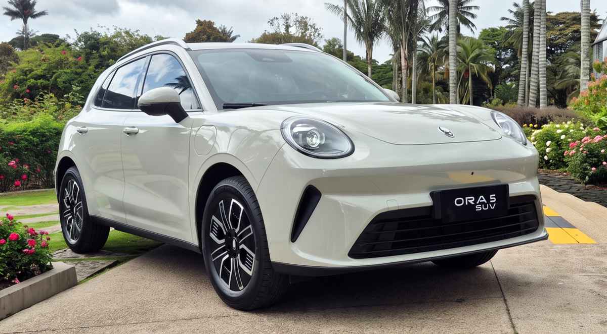 Vista frontal tres cuartos de la nueva SUV eléctrica GWM Ora 5 en color blanco marfil, estacionada sobre un camino de piedra rodeado de jardines, destacando su capó curvo y sus característicos faros redondos de estilo retro.