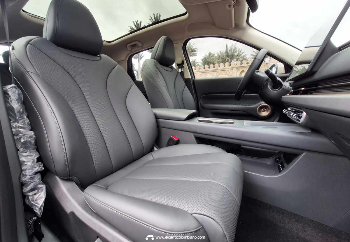 Asientos delanteros de la SUV GWM Ora 5 tapizados en cuero gris con finas perforaciones, destacando el diseño de los soportes laterales, los ajustes eléctricos y la continuidad del diseño elegante hacia la puerta del conductor.