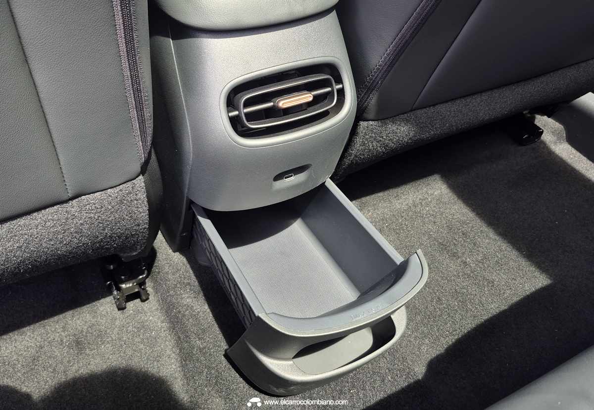 Detalle funcional de la consola central posterior de la GWM Ora 5, mostrando una salida de aire acondicionado con borde cobrizo, un puerto de carga USB tipo C y una pequeña gaveta o cajón deslizable abierto.